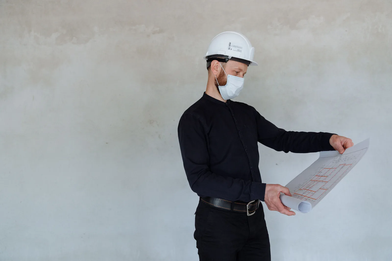 Architect in safety helmet and mask reviewing building plans indoors. What zoning and permits rules require from building, fire, health and land-use reviewers?