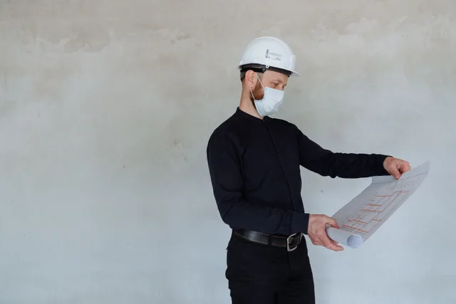 Architect in safety helmet and mask reviewing building plans indoors. What zoning and permits rules require from building, fire, health and land-use reviewers?